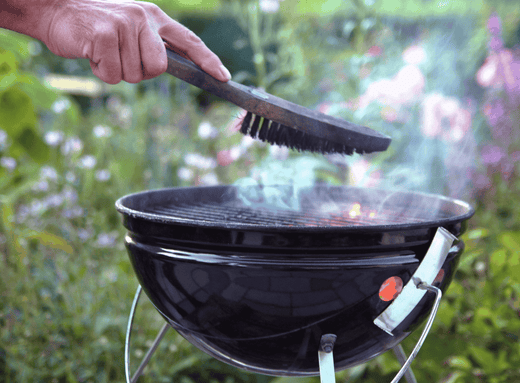 hand holding a wire brush over a charcoal grill