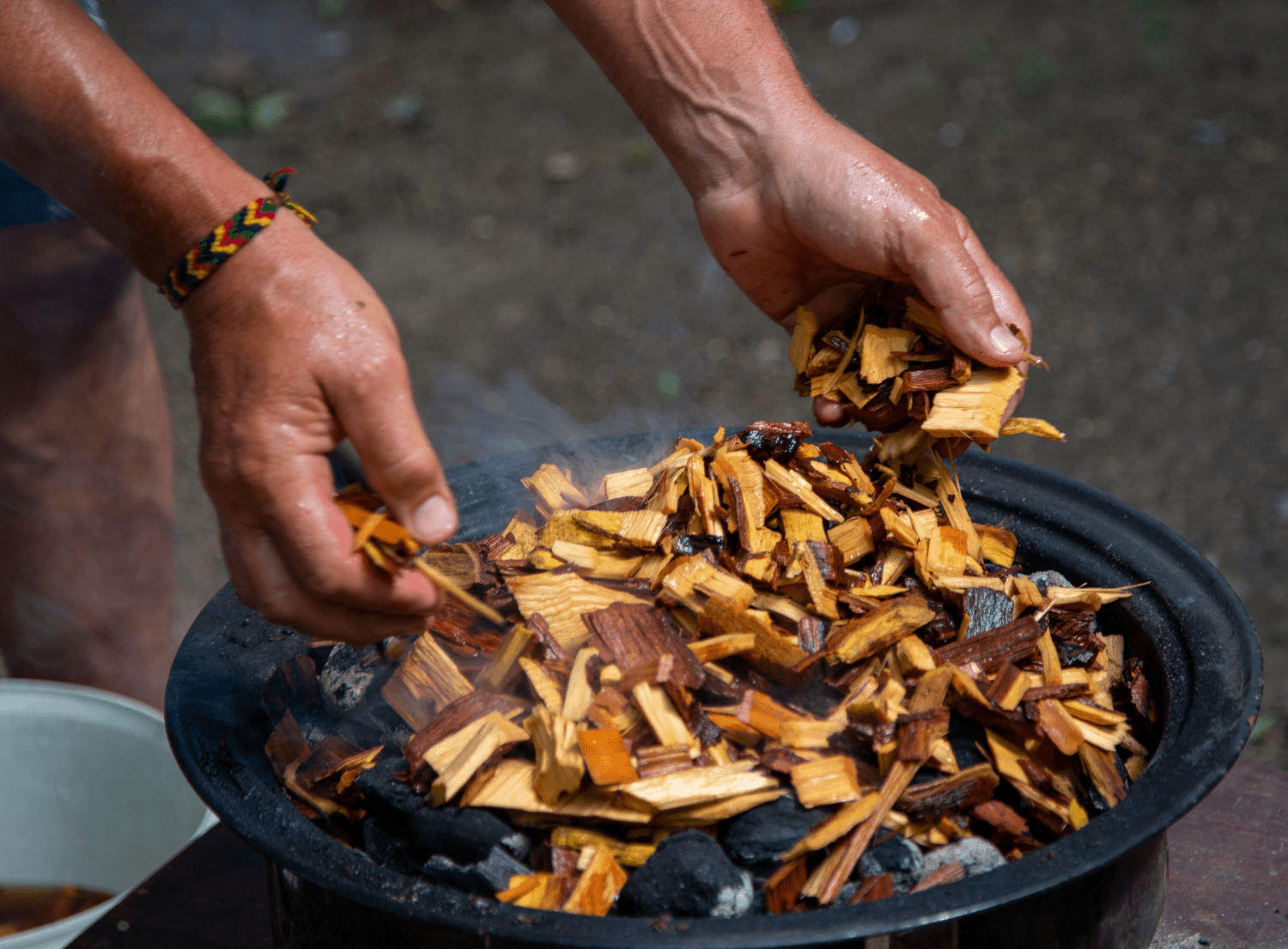 person putting wood chips on charcoal grill