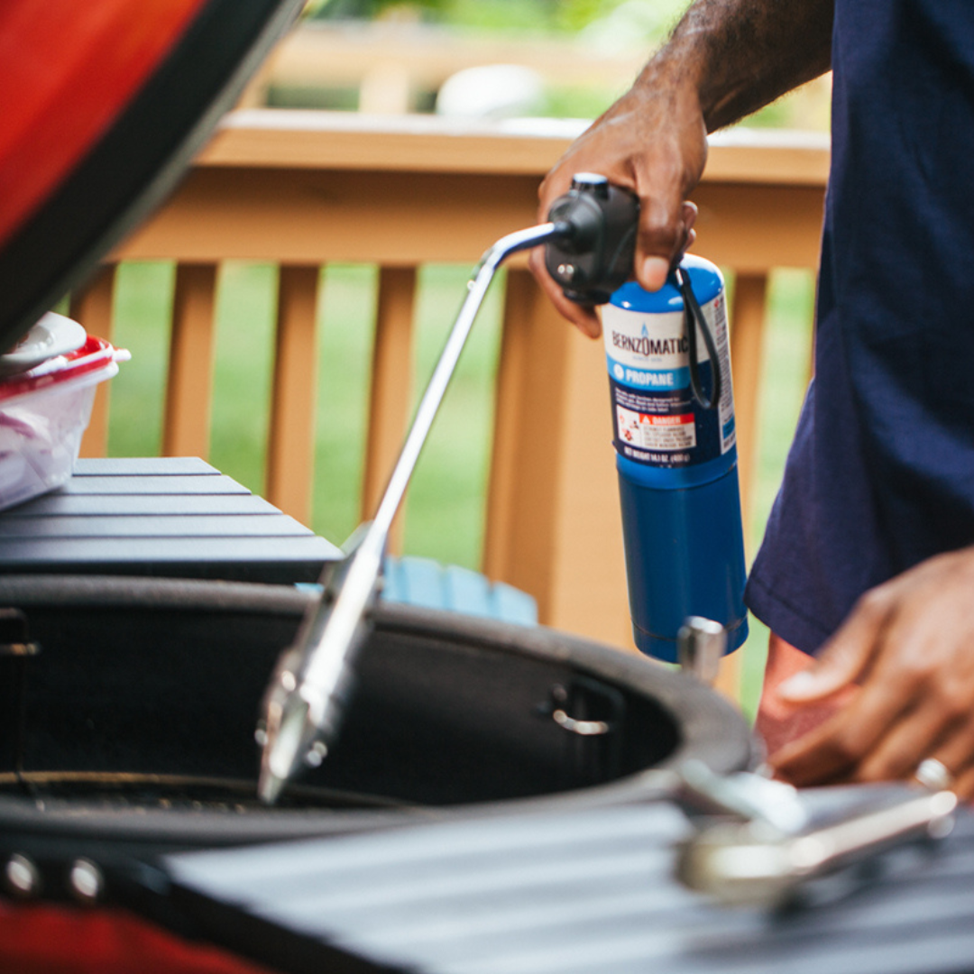 Man at kamado joe on deck, lighting grill with rocketfire torch attached to propane tank