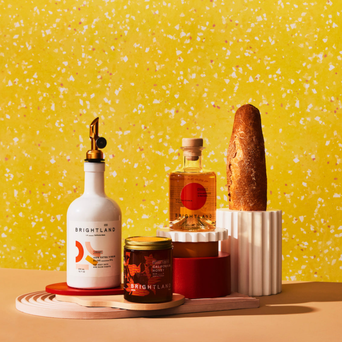 Assorted products including a bottle, jar, and loaf of bread on a yellow speckled background