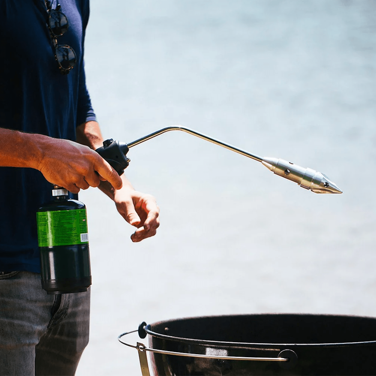 Man with blue shirt and jeans holding out rocketfire over charcoal grill outside