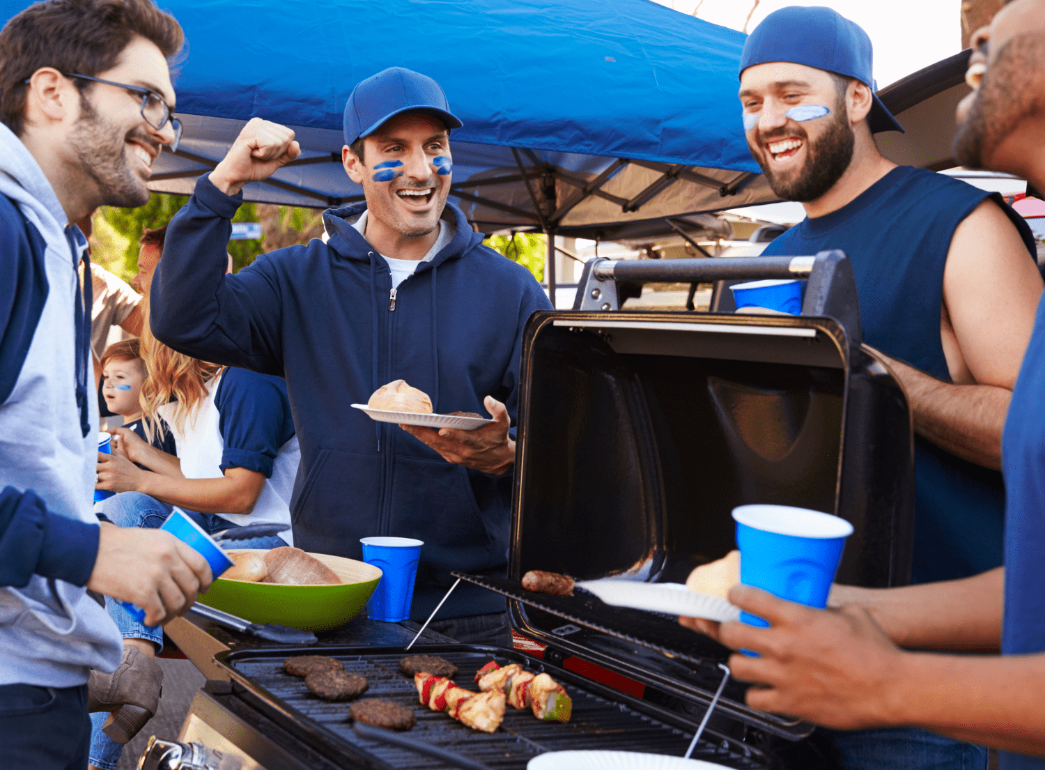group of four males dressed in blue cheering by the grill