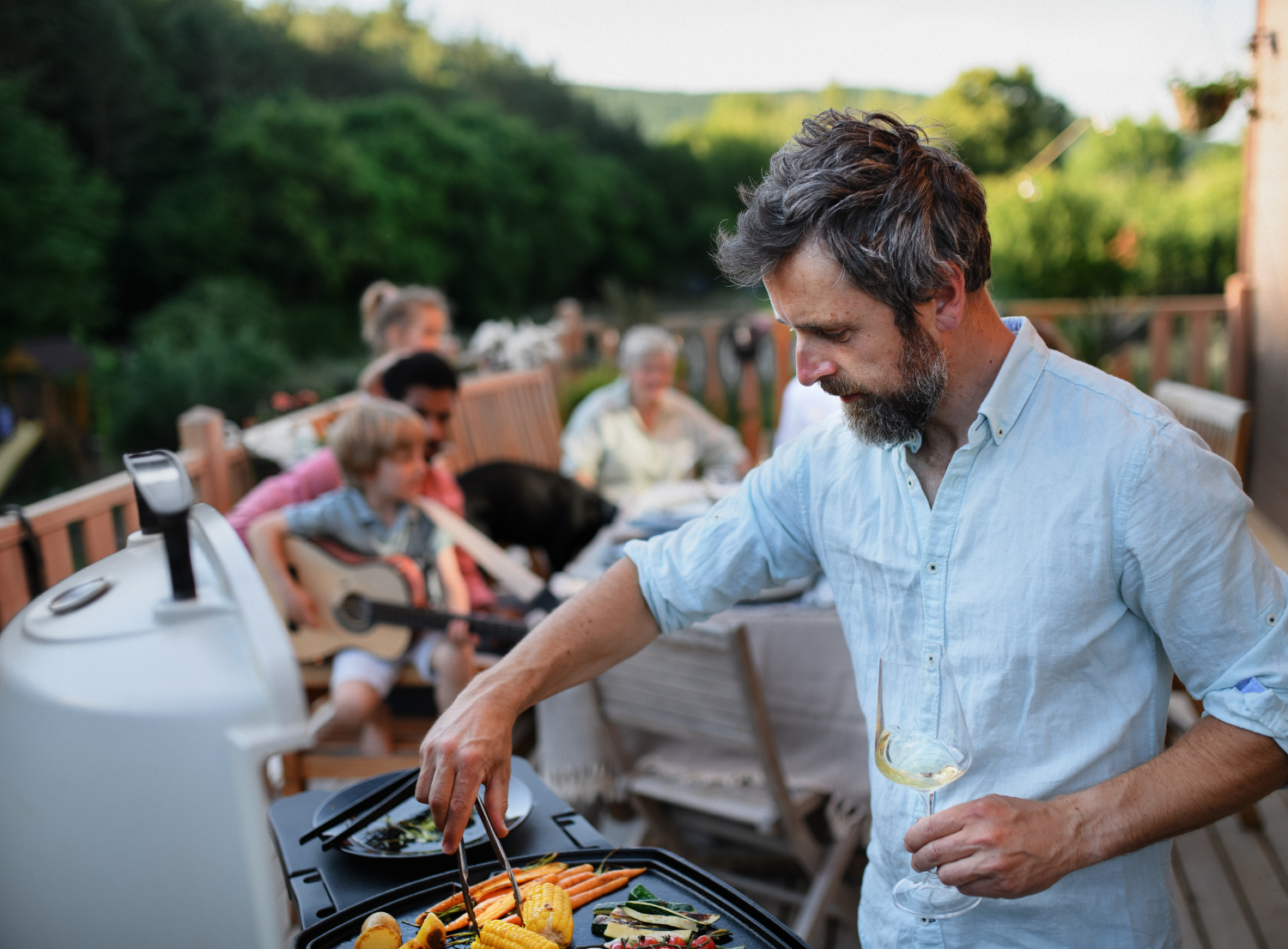 Man grilling vegetables on the bbq with his friends sitting behind him