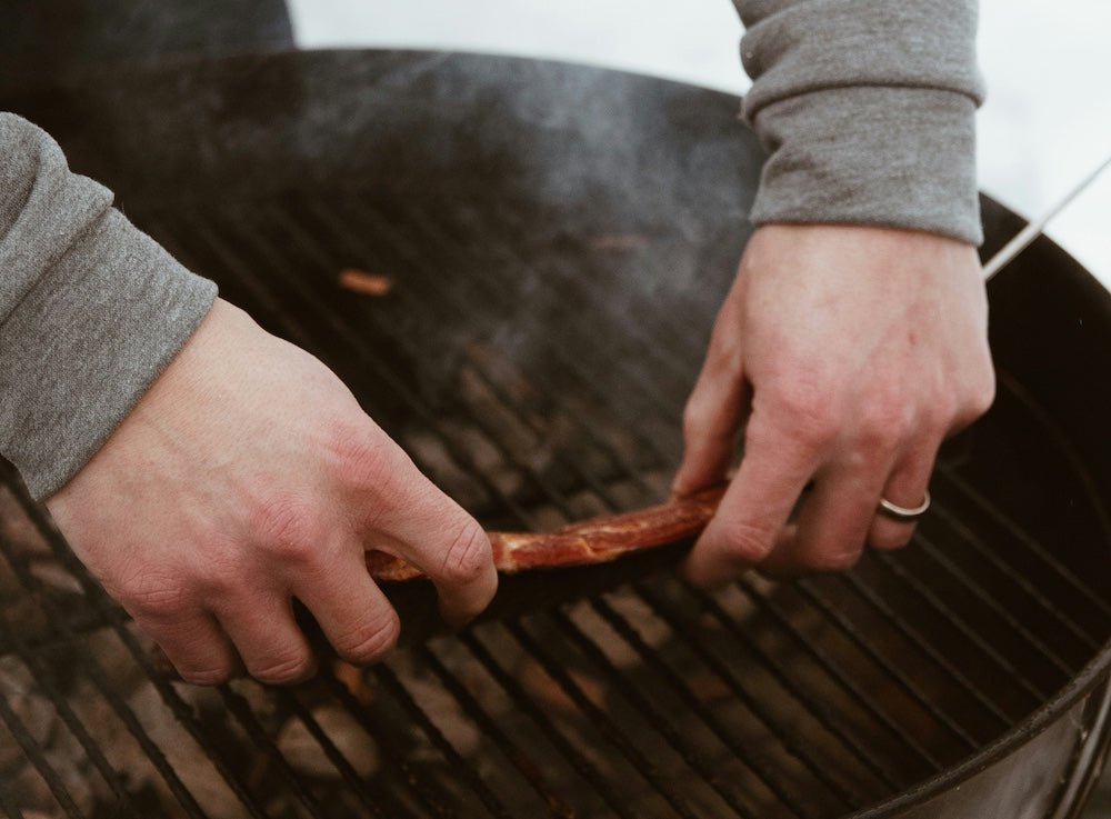 Man placing meat on lit charcoal grill - best charcoal lighter fluid